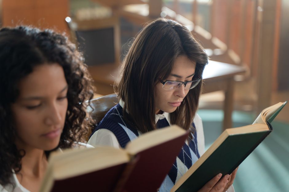 Two young women reading books in a library