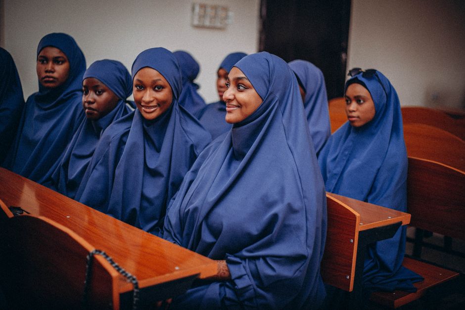 Group of young women in blue garments sitting attentively indoors.