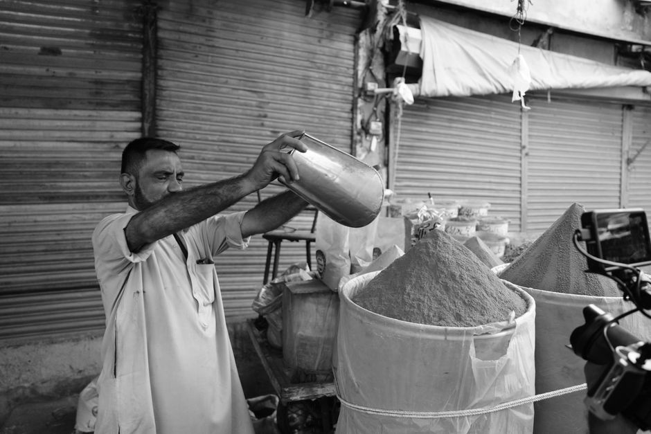 A local vendor measuring spices in an outdoor market setting, depicting daily life and commerce.