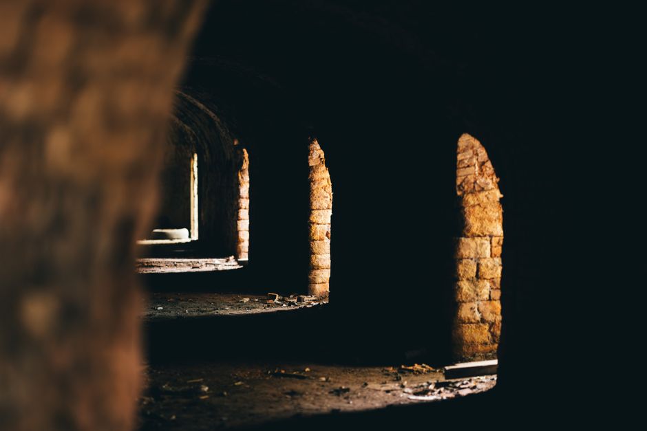 Explore an eerie abandoned corridor with ancient stone arches and play of light and shadow.
