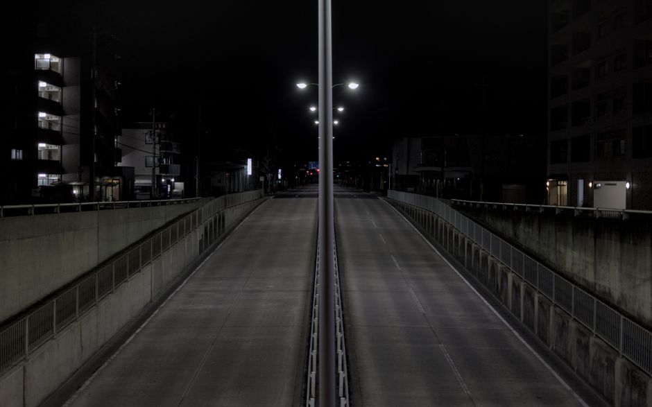 A deserted city highway at night lined with streetlights and urban buildings, showcasing solitude.