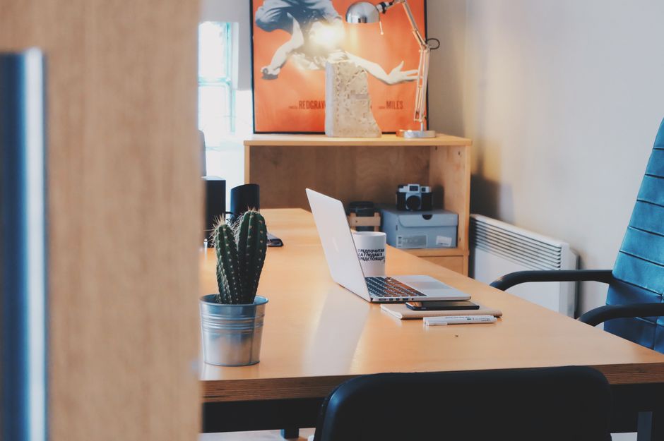 A modern office desk setup featuring a cactus plant, laptop, and stylish decor in a contemporary office space.