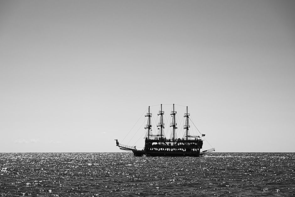 Black and white photo of a sailing ship on the shimmering ocean horizon.