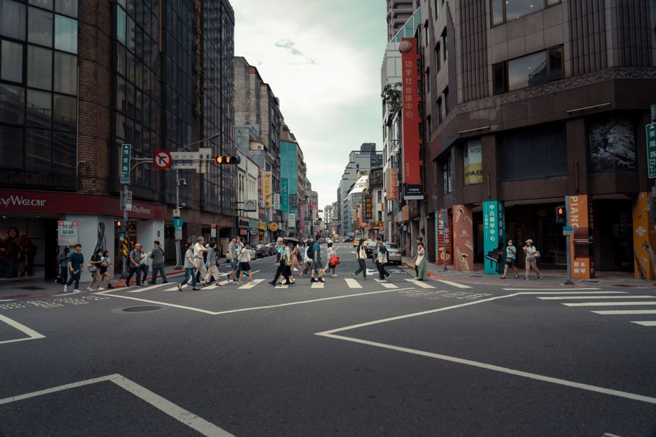 A busy urban intersection with people crossing surrounded by modern buildings, showcasing city life.