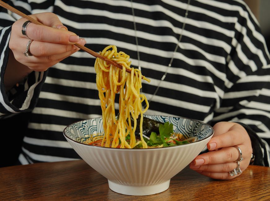 Close-up of a person eating ramen noodles with chopsticks.