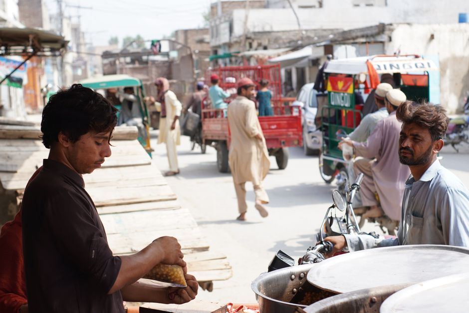 Street vendor selling food in bustling Nowshera, Pakistan. Urban life depicted with locals.