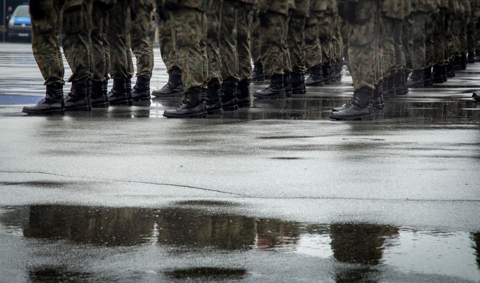 Group of soldiers in uniform standing on wet asphalt, reflections visible.
