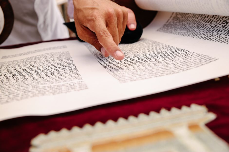A close-up view of a hand pointing to text on an ancient religious scroll, indicating reading and study.