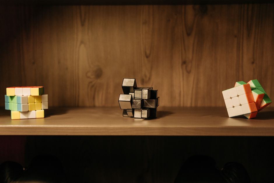 A collection of various Rubik's cubes displayed on a wooden shelf, showcasing unique designs and patterns.