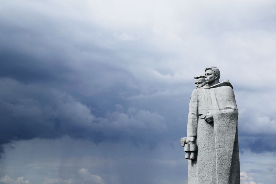 Imposing monument of two figures with binoculars set against a stormy sky.