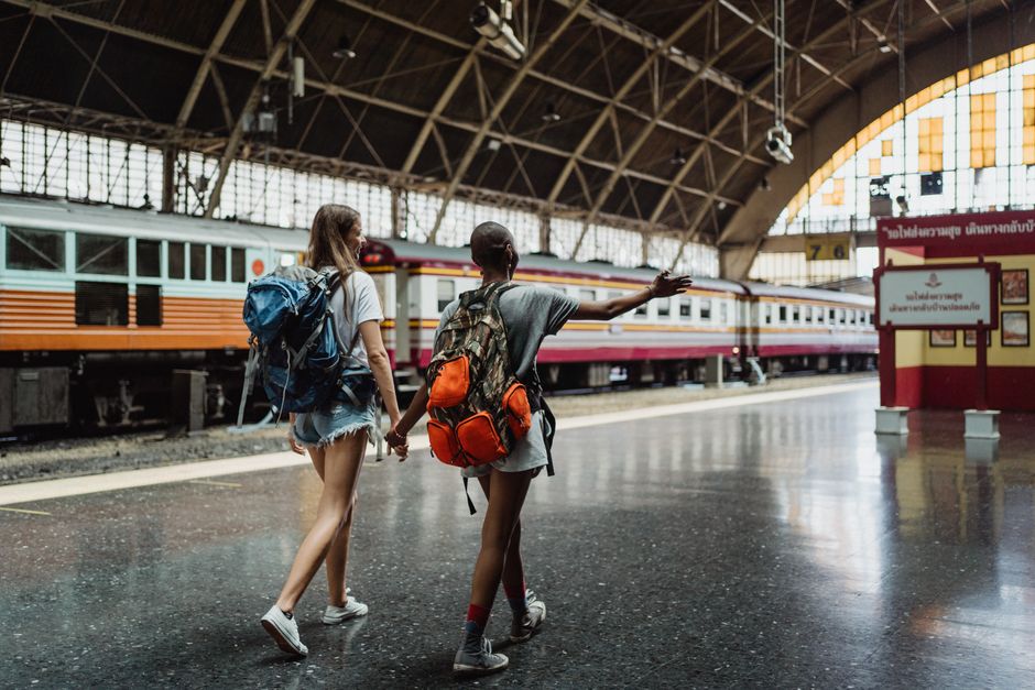 Two women with backpacks walking through a train station, showcasing adventure and friendship.
