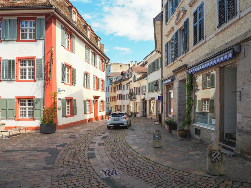 A picturesque European street with historical buildings, cobblestones, and a car passing by.