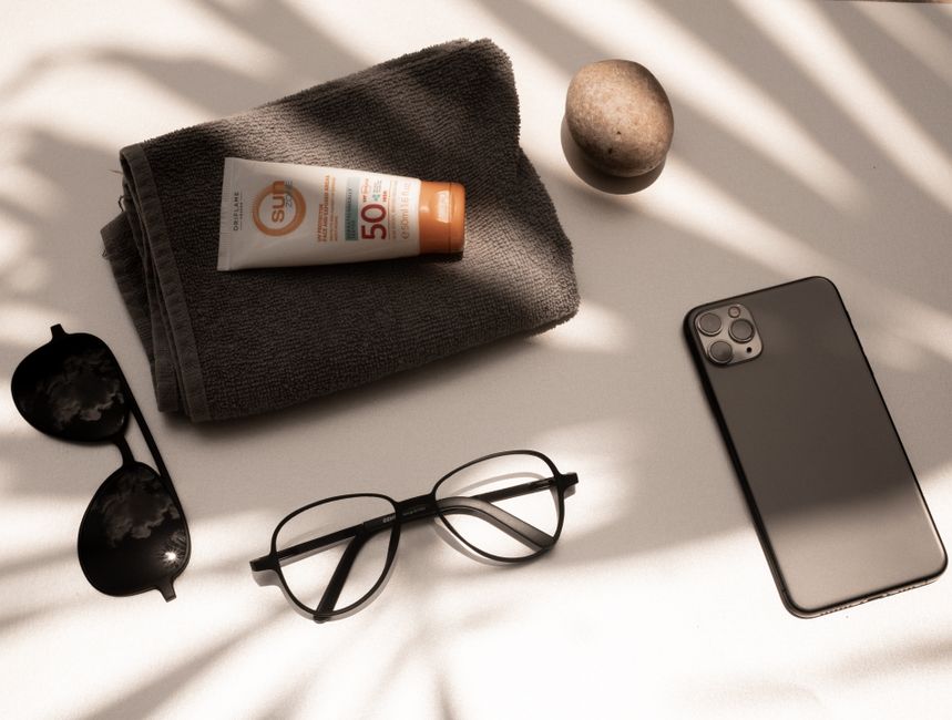 Flat lay of summer essentials: sunscreen, glasses, smartphone, and towel under sunlight in Yucatan, Mexico.