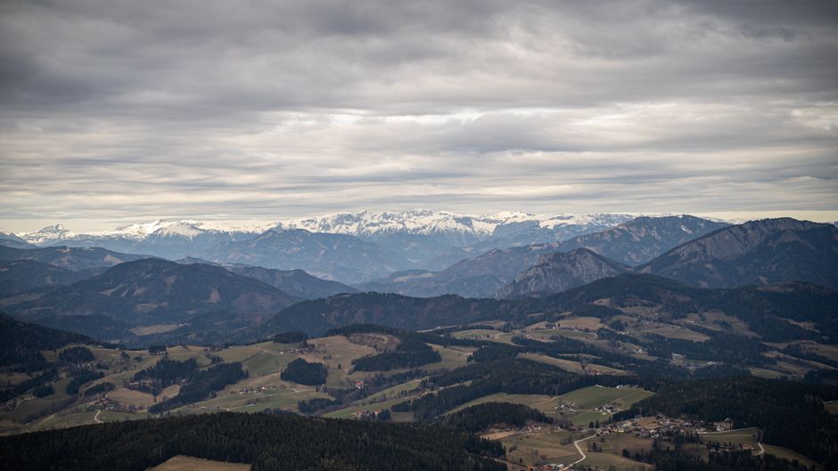 Aerial view of picturesque mountain range with snow-capped peaks under cloudy skies.