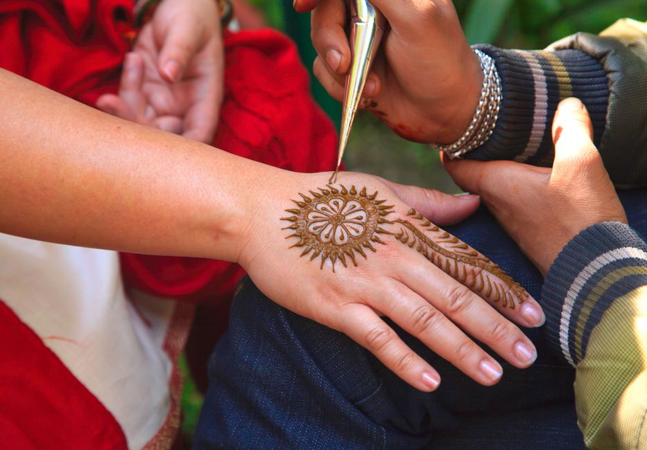 Woman getting an intricate henna design applied to her hand in a close-up shot.