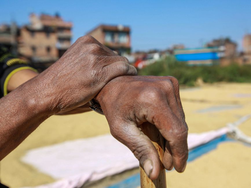 Detailed close-up of elderly hands holding a stick outdoors against a blurred urban backdrop.