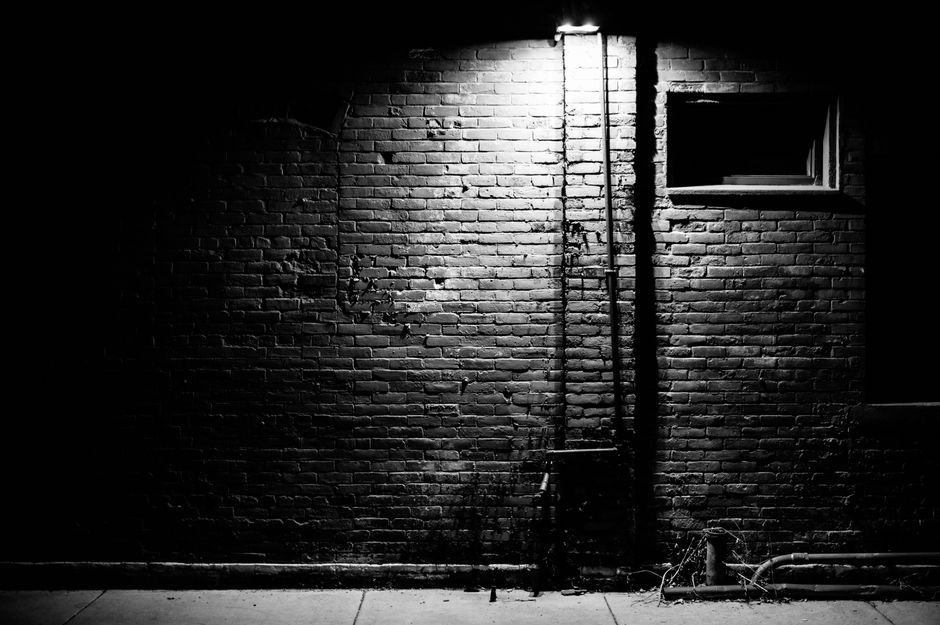 Black and white of aged building with brick walls in bright light of streetlamp