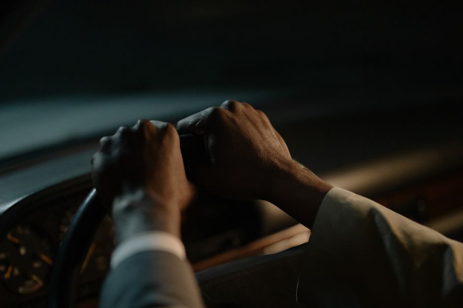 A driver's hands grasp the steering wheel in a dimly-lit vehicle interior, conveying focus and control.
