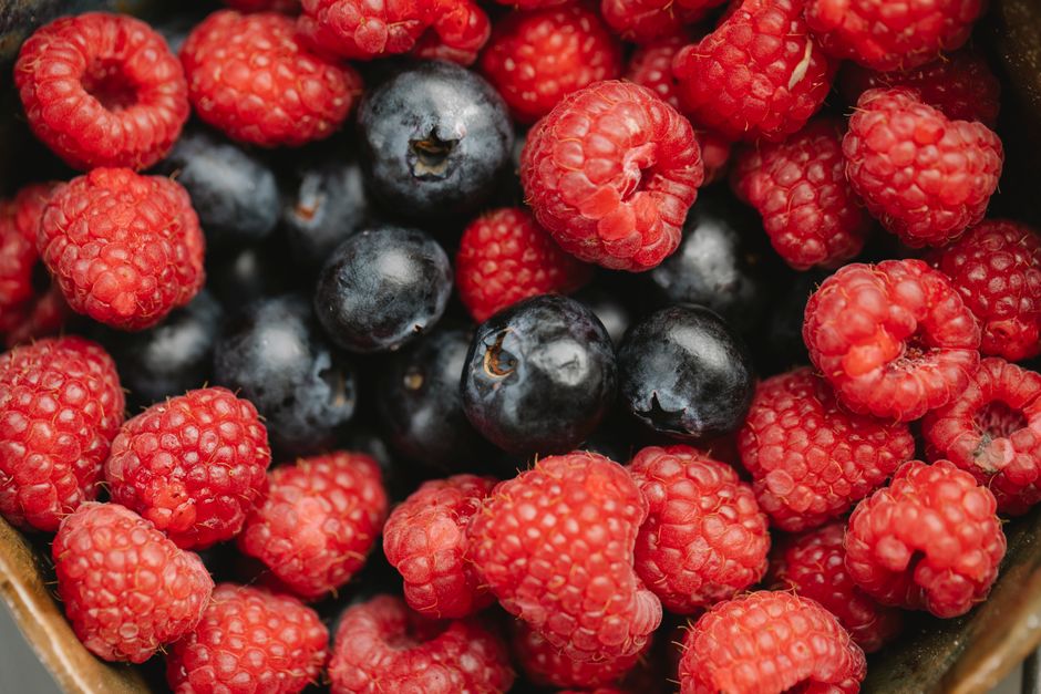 Closeup heap of delicious fresh raspberries and blueberries picked from garden placed in bowl during harvest season in summer