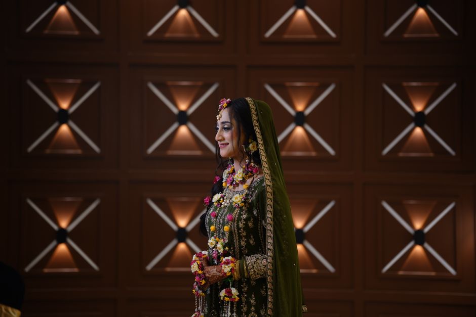 Beautiful bride in traditional green attire with floral jewelry, set against a decorative backdrop indoors.