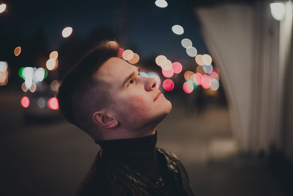 Young man looking up in a city at night. Bokeh lights create a dreamy atmosphere.