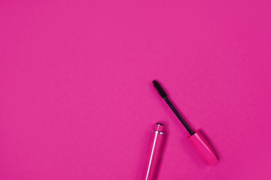 Close-up of an open mascara on a bright pink background, perfect for beauty and fashion themes.
