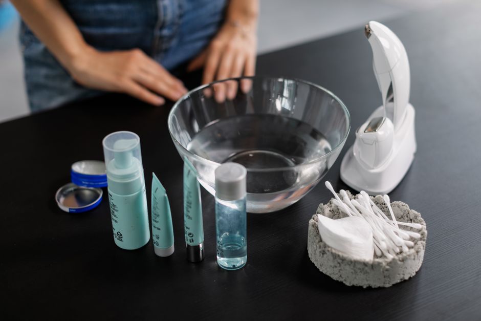 Flat lay of skincare products, tools, and a glass bowl on a black surface for beauty care routines.
