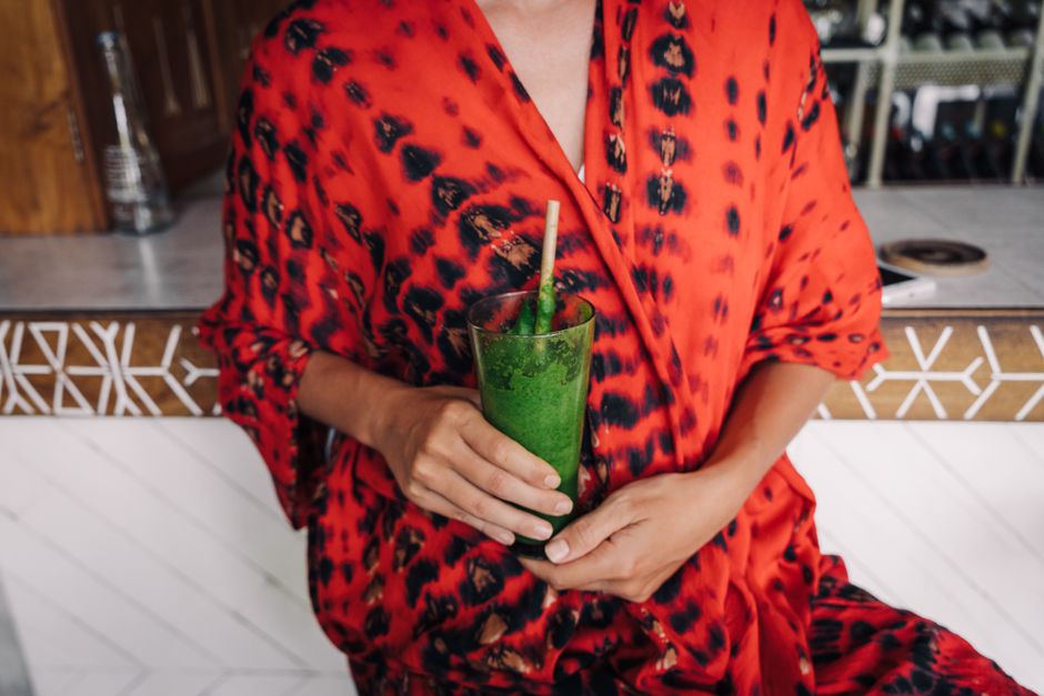 Close-up of a person holding a green smoothie in a chic bar setting, wearing a vibrant red robe.