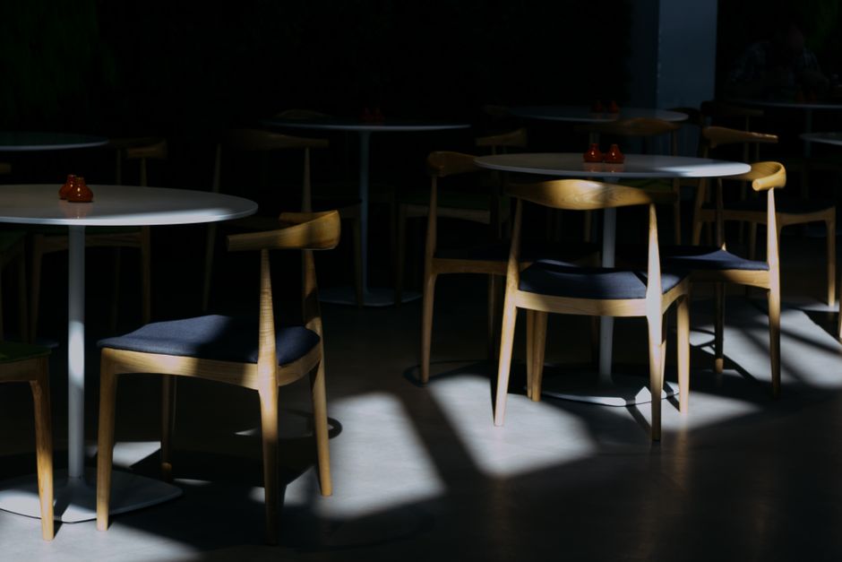 A dimly lit indoor cafe features sunlight casting shadows on modern chairs and tables.