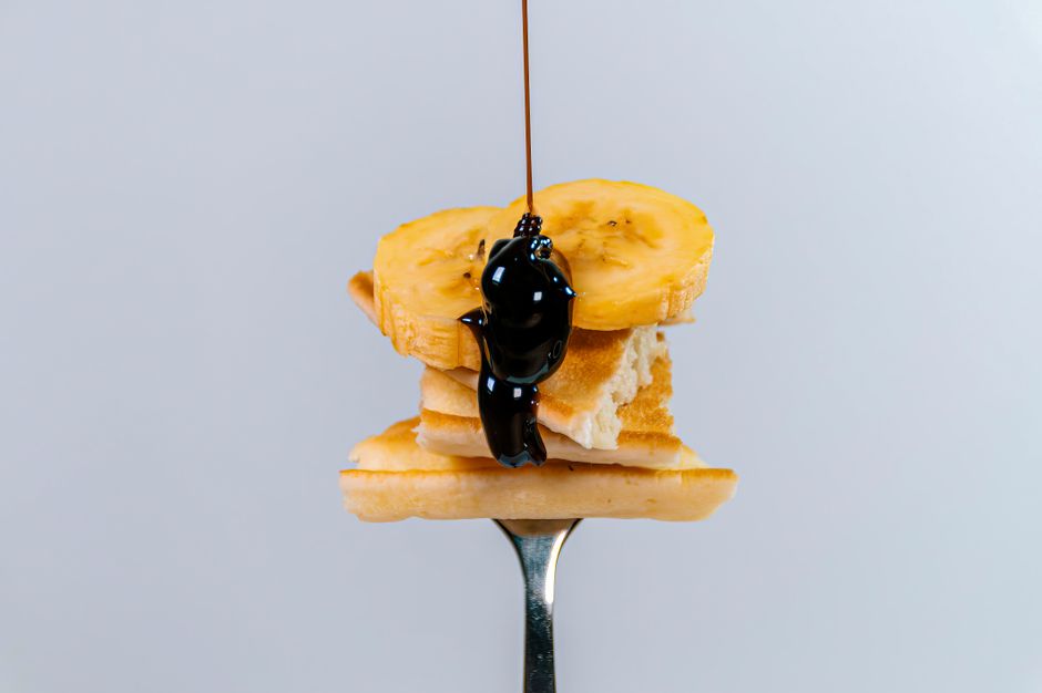 Close-up of banana slices on pancake with chocolate syrup on a fork. Minimalist, appetizing shot.