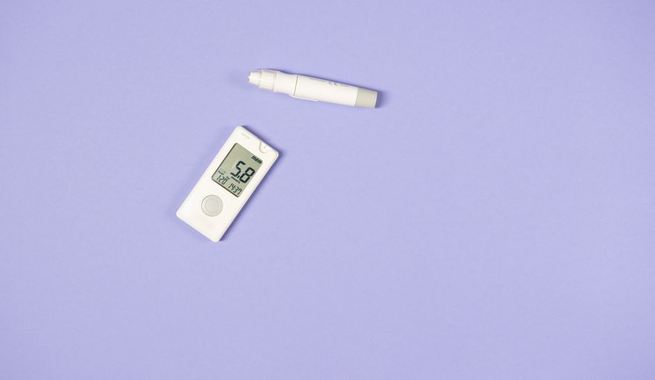 White glucometer and lancet pen on light purple background for diabetes management.