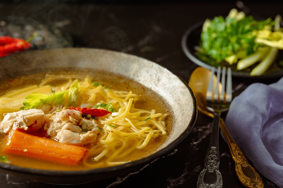 Capture of a flavorful chicken noodle soup with garnishes in a rustic setting.