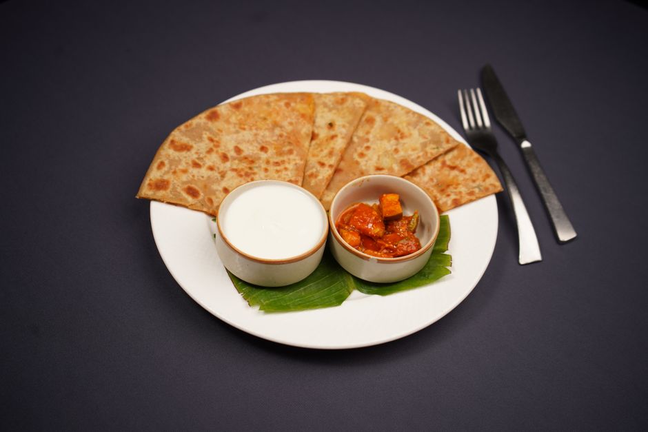 Tasty Indian paratha served with pickle and yogurt on a white plate with cutlery.