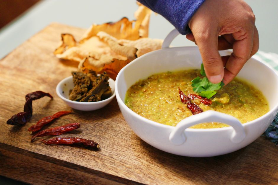 Hand garnishing a bowl of spicy khichdi with fresh coriander leaves.