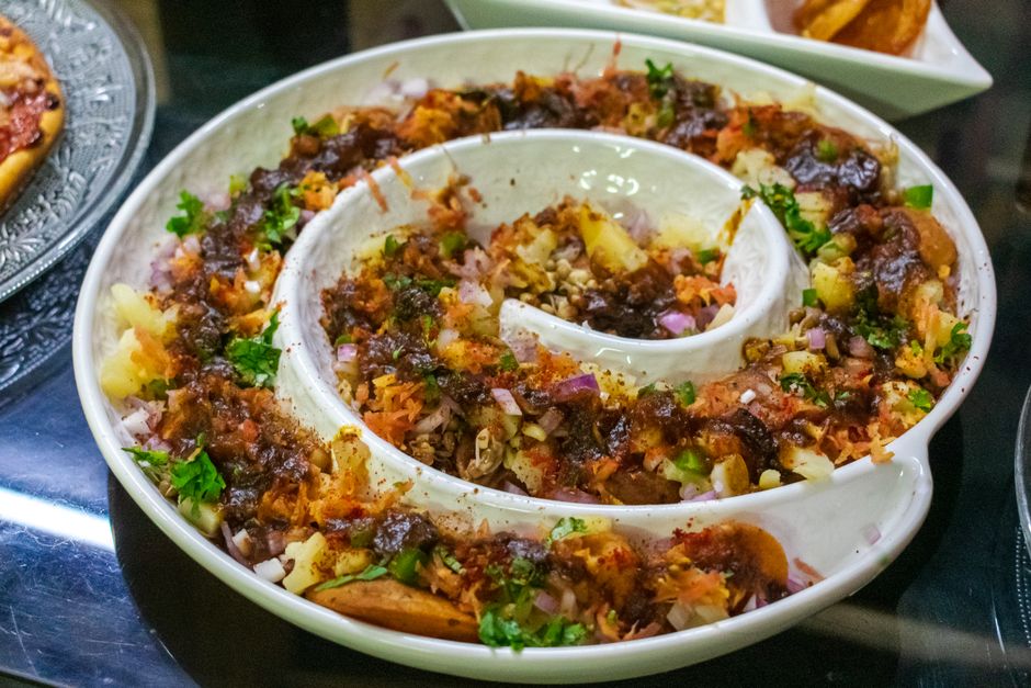 A vibrant and colorful spiral platter of Indian Aloo Chaat garnished with herbs.