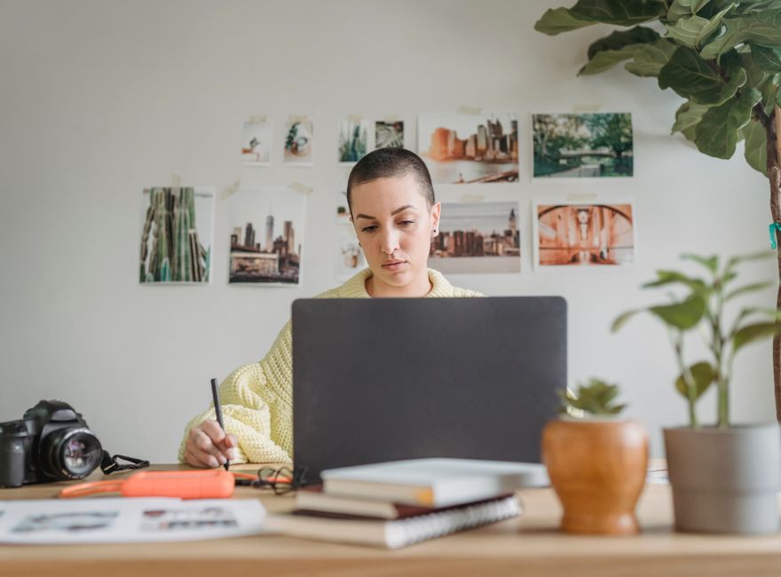 Professional female designer looking at laptop and using graphic tablet while sitting at table in light workspace