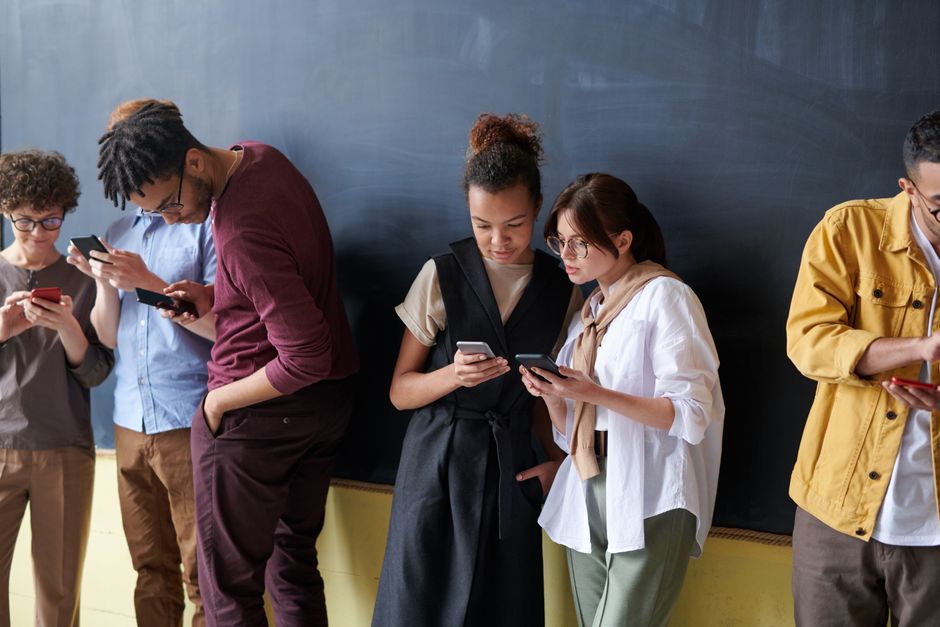 A diverse group of young adults using smartphones in a casual indoor setting.