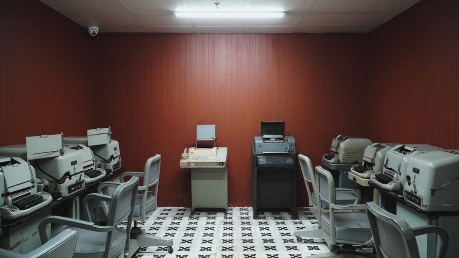 An empty room filled with vintage teletype machines and retro decor, conveying an old-world tech vibe.