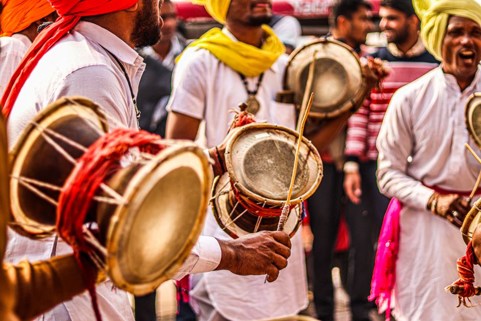 A lively scene of men playing traditional drums at a cultural festival, wearing colorful attire.