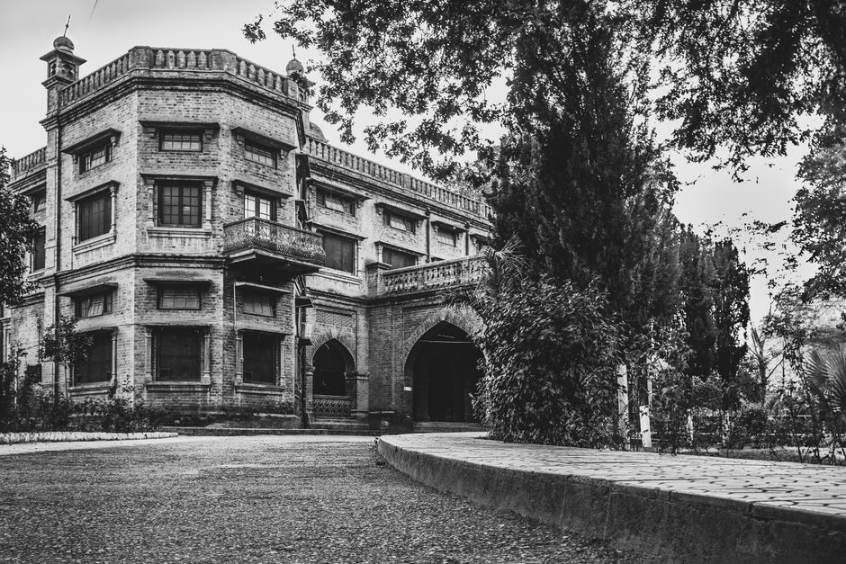Black and white photograph of a historic building facade in Pakistan, showcasing architectural design and greenery.