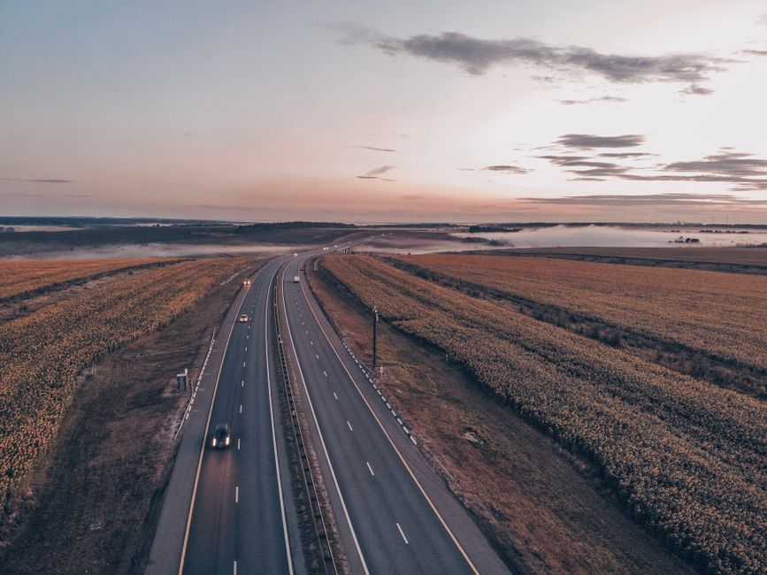Aerial view of a tranquil rural highway surrounded by fields during sunset, capturing the serene landscape.