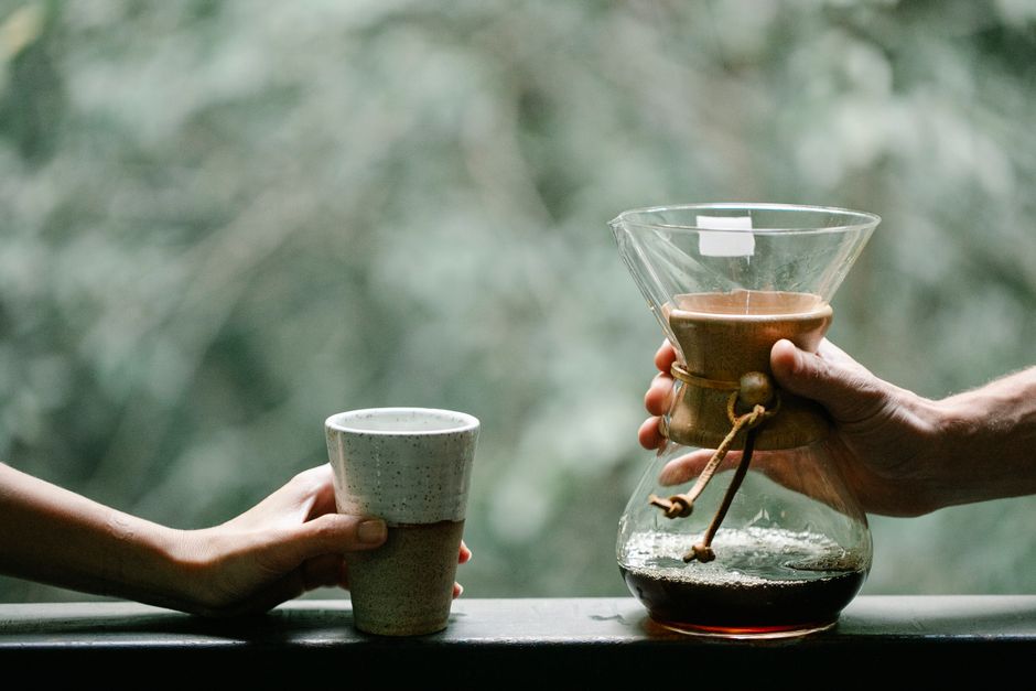 Crop unrecognizable girlfriend and boyfriend with hot drink in glass and Chemex coffee maker on terrace in countryside