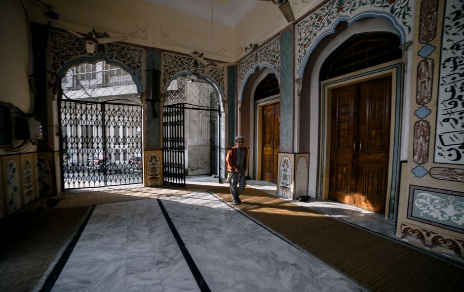 A man walks inside a traditional Pakistani mosque with intricate decor and wooden doors.
