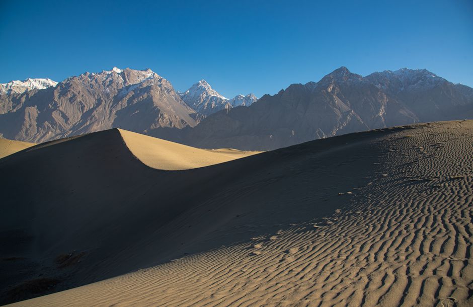 Stunning dune landscape against snow-capped mountains in Skardu, offering a breathtaking natural vista.