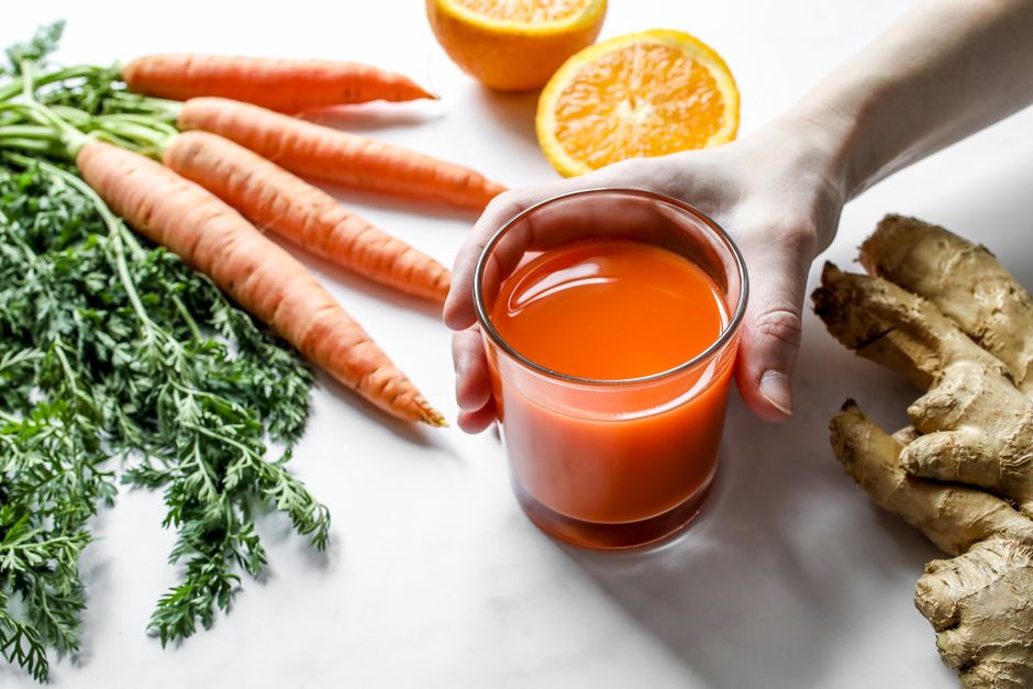 Vibrant carrot and ginger juice surrounded by fresh ingredients on a clean surface.