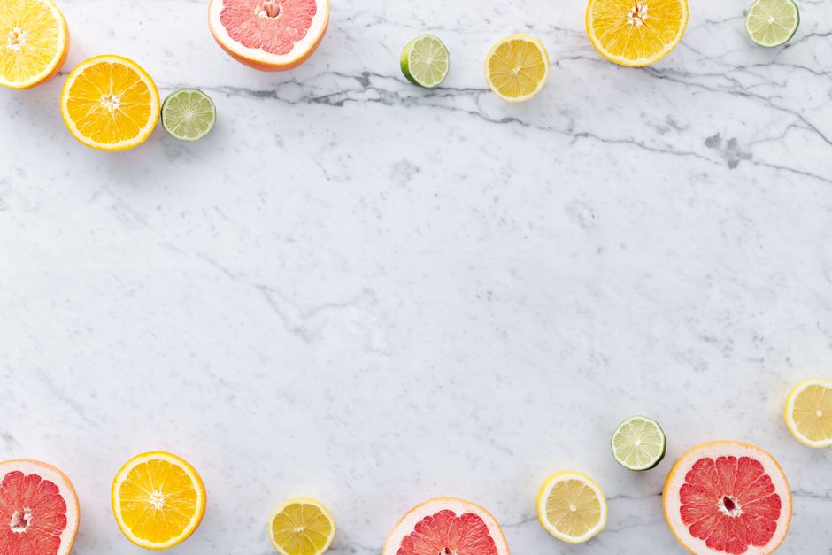 Flat lay of assorted citrus slices on a marble surface with ample copy space.