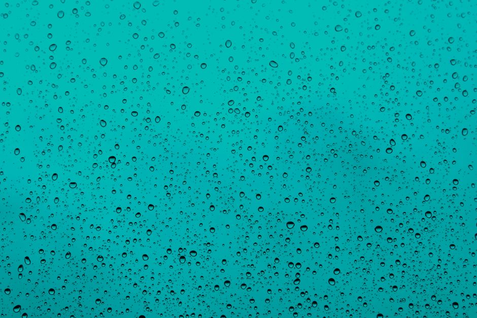 Close-up of water droplets on a teal glass window, capturing the beauty of rain.