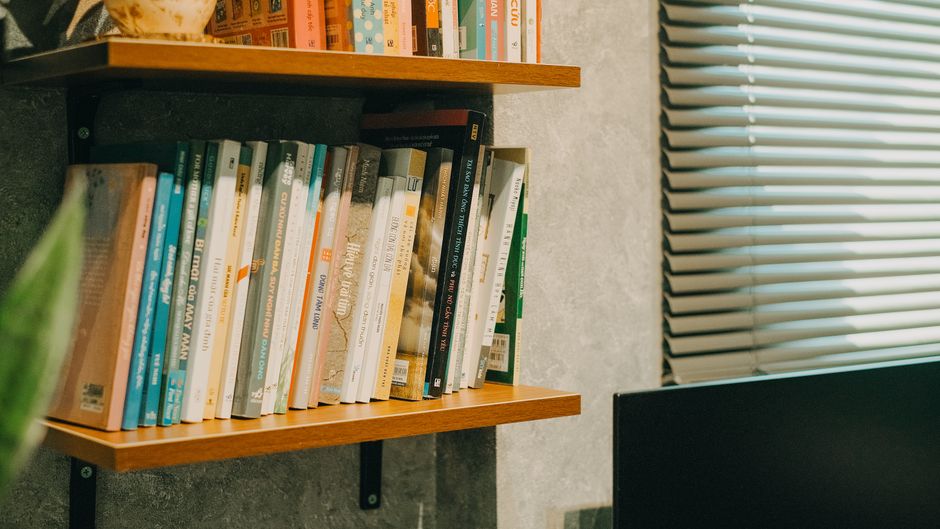 Books neatly arranged on a wooden shelf in a modern indoor space with natural light.