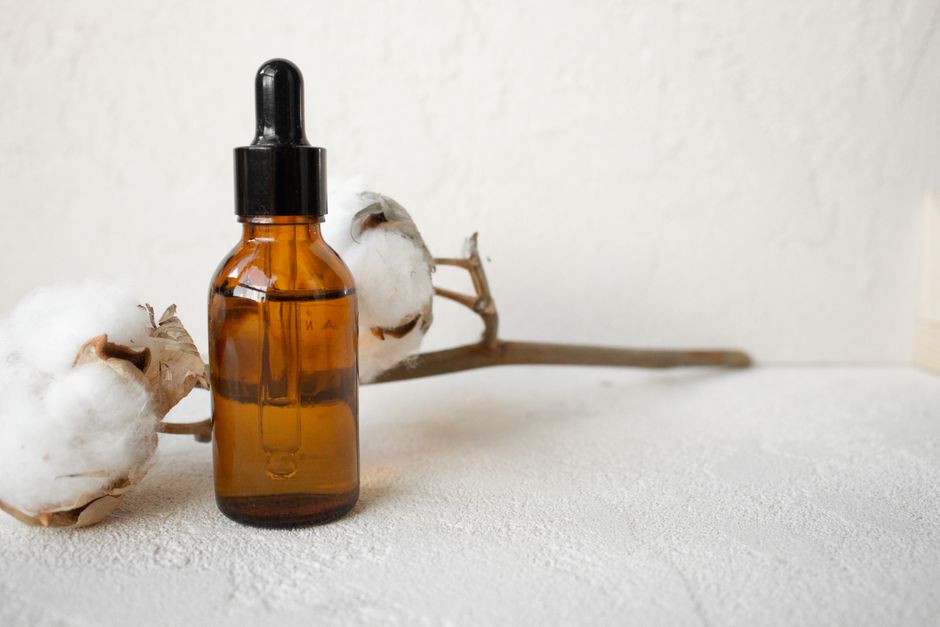 Brown glass dropper bottle with cotton branch on white textured surface.