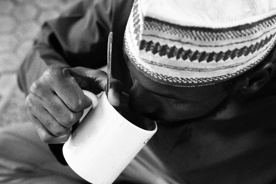 A man in traditional attire drinking from a mug, captured in black and white.